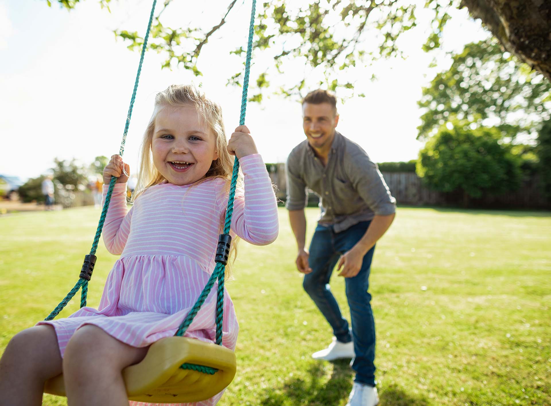 Vater gibt der Schaukel anschwung auf dem seine kleine lächelnde Tochter sitzt